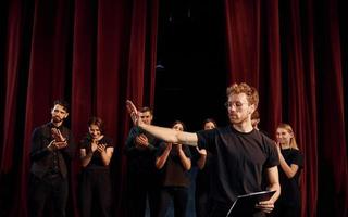 Man with notepad practice his role. Group of actors in dark colored clothes on rehearsal in the theater photo