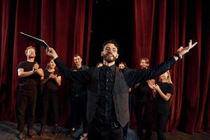 Expressionalible guy practicing his role. Group of actors in dark colored clothes on rehearsal in the theater photo