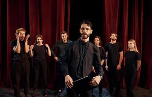 Expressionalible guy practicing his role. Group of actors in dark colored clothes on rehearsal in the theater photo