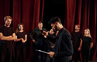 Expressionalible guy practicing his role. Group of actors in dark colored clothes on rehearsal in the theater photo