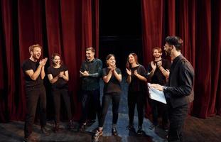 Man is practicing his role. Group of actors in dark colored clothes on rehearsal in the theater photo