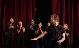 hombre con bloc de notas practica su papel. grupo de actores con ropa de color oscuro ensayando en el teatro foto