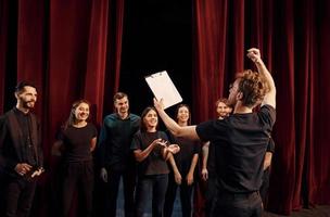 hombre con bloc de notas practica su papel. grupo de actores con ropa de color oscuro ensayando en el teatro foto