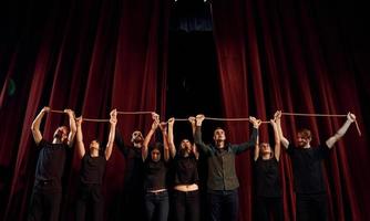 sosteniendo la cuerda en las manos por encima de la cabeza. grupo de actores con ropa de color oscuro ensayando en el teatro foto