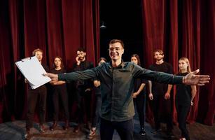 Man is practicing his role. Group of actors in dark colored clothes on rehearsal in the theater photo