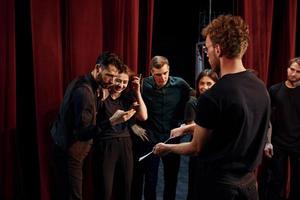 Man with notepad practice his role. Group of actors in dark colored clothes on rehearsal in the theater photo