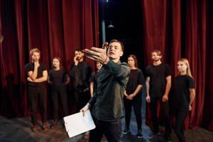 Man is practicing his role. Group of actors in dark colored clothes on rehearsal in the theater photo