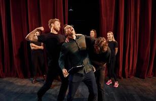 escena de lucha. grupo de actores con ropa de color oscuro ensayando en el teatro foto