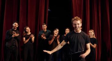 Man with notepad practice his role. Group of actors in dark colored clothes on rehearsal in the theater photo