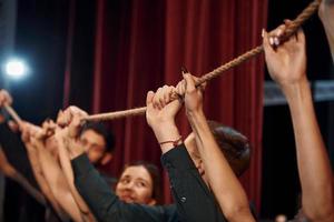 sosteniendo la cuerda en las manos por encima de la cabeza. grupo de actores con ropa de color oscuro ensayando en el teatro foto