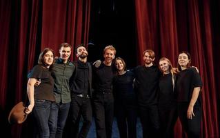 de pie contra las cortinas rojas. grupo de actores con ropa de color oscuro ensayando en el teatro foto