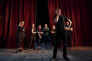 Man standing against people. Group of actors in dark colored clothes on rehearsal in the theater photo