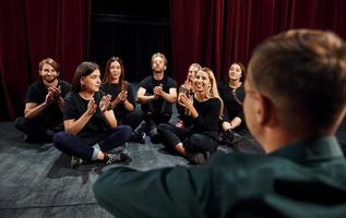 Sitting on the floor. Group of actors in dark colored clothes on rehearsal in the theater photo