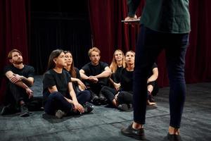 Sitting and listening to man. Group of actors in dark colored clothes on rehearsal in the theater photo