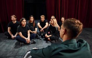 Sitting on the floor. Group of actors in dark colored clothes on rehearsal in the theater photo