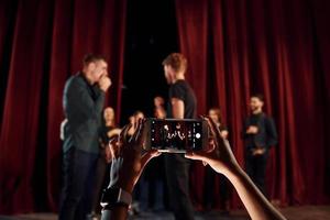 las manos de la mujer sostienen el teléfono y toman fotos. grupo de actores con ropa de color oscuro ensayando en el teatro foto