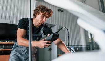 Tests car's electronics. Adult man in grey colored uniform works in the automobile salon photo