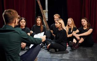 Sitting on the floor. Group of actors in dark colored clothes on rehearsal in the theater photo