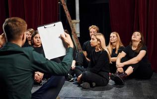 Sitting on the floor. Group of actors in dark colored clothes on rehearsal in the theater photo