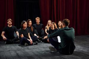 Sitting on the floor. Group of actors in dark colored clothes on rehearsal in the theater photo