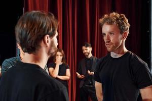 Two people talking. Group of actors in dark colored clothes on rehearsal in the theater photo