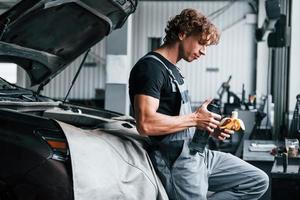 Takes a break. Eats banana and drinks water. Adult man in grey colored uniform works in the automobile salon photo