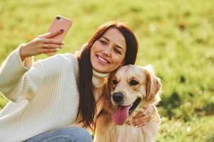Making selfie. Young woman have a walk with Golden Retriever in the park photo