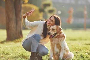 Making selfie. Young woman have a walk with Golden Retriever in the park photo