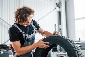 Fixes broken tire. Adult man in grey colored uniform works in the automobile salon photo