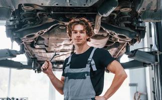 hombre adulto guapo con uniforme de color gris parado debajo del automóvil foto