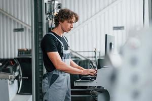 Using computer. Adult man in grey colored uniform works in the automobile salon photo