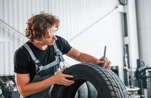 Fixes broken tire. Adult man in grey colored uniform works in the automobile salon photo