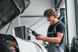 Special tool for testing characteristics. Adult man in grey colored uniform works in the automobile salon photo