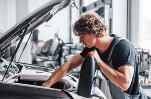 Changing oil. Adult man in grey colored uniform works in the automobile salon photo