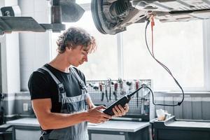 herramienta especial para probar características. hombre adulto con uniforme de color gris trabaja en el salón del automóvil foto