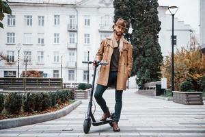 en el scooter eléctrico. modelo masculino joven en ropa de moda está al aire libre en la ciudad durante el día foto