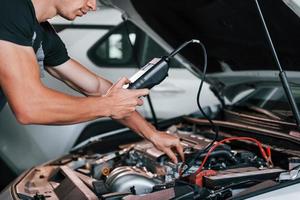 Tests car's electronics. Adult man in grey colored uniform works in the automobile salon photo