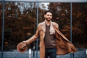 de pie contra el edificio con puertas de vidrio. modelo masculino joven en ropa de moda está al aire libre en la ciudad durante el día foto