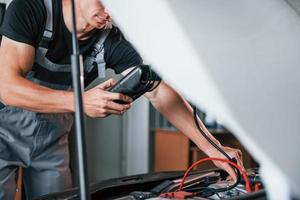 Tests car's electronics. Adult man in grey colored uniform works in the automobile salon photo