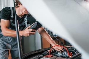 Tests car's electronics. Adult man in grey colored uniform works in the automobile salon photo