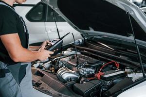 Special tool for testing characteristics. Adult man in grey colored uniform works in the automobile salon photo