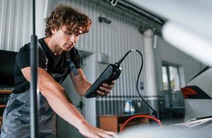 Tests car's electronics. Adult man in grey colored uniform works in the automobile salon photo