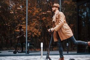 montando scooter eléctrico. modelo masculino joven en ropa de moda está al aire libre en la ciudad durante el día foto