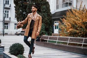 tiene sombrero y posando. modelo masculino joven en ropa de moda está al aire libre en la ciudad durante el día foto