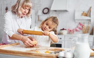 Kneads the dough. Senior grandmother with her little granddaughter cooks sweets for Christmas on the kitchen photo