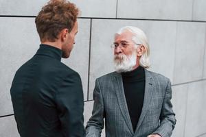 Young guy with senior man in elegant clothes is outdoors together. Conception of business photo