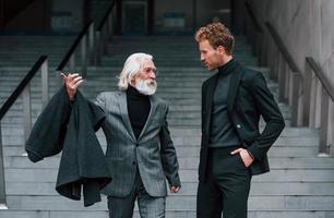 caminando por las escaleras. un joven con un anciano vestido con ropa elegante está juntos al aire libre. concepción del negocio foto