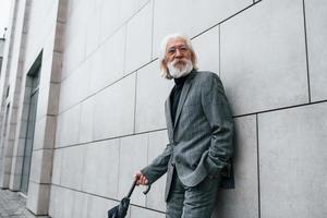 Holds umbrella. Senior businessman in formal clothes, with grey hair and beard is outdoors photo