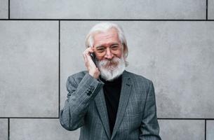 Senior businessman in formal clothes, with grey hair and beard is outdoors talks by phone photo
