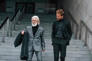 caminando por las escaleras. un joven con un anciano vestido con ropa elegante está juntos al aire libre. concepción del negocio foto